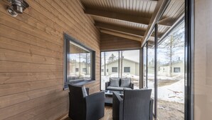 A wooden interior with a large window, wicker furniture, and a view of a snowy yard. - Holiday Club Kuusamon Tropiikki (Kuusamo)