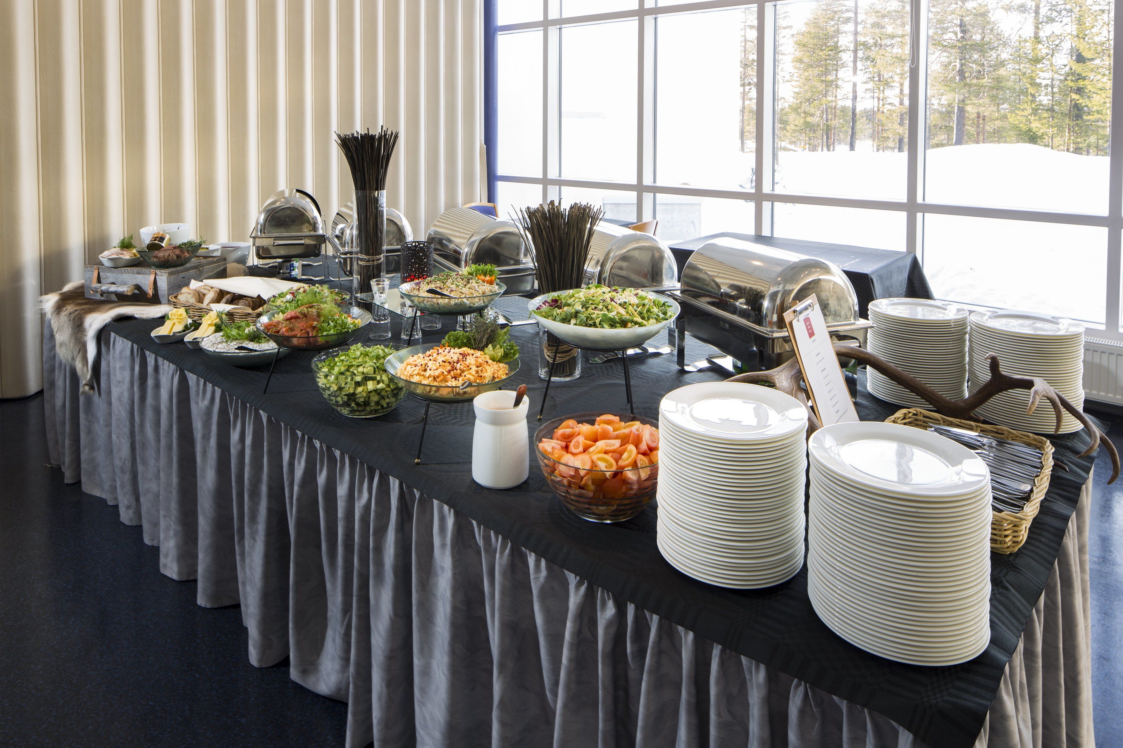 A buffet table with various food items and utensils, set against a window with a snowy view.