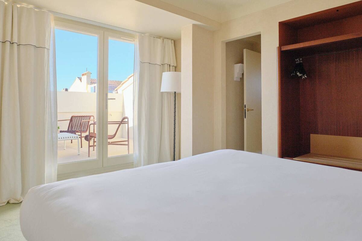 Habitación de hotel con una cama grande, un armario de madera, una puerta corrediza de vidrio que da a un área de estar al aire libre y una lámpara.
