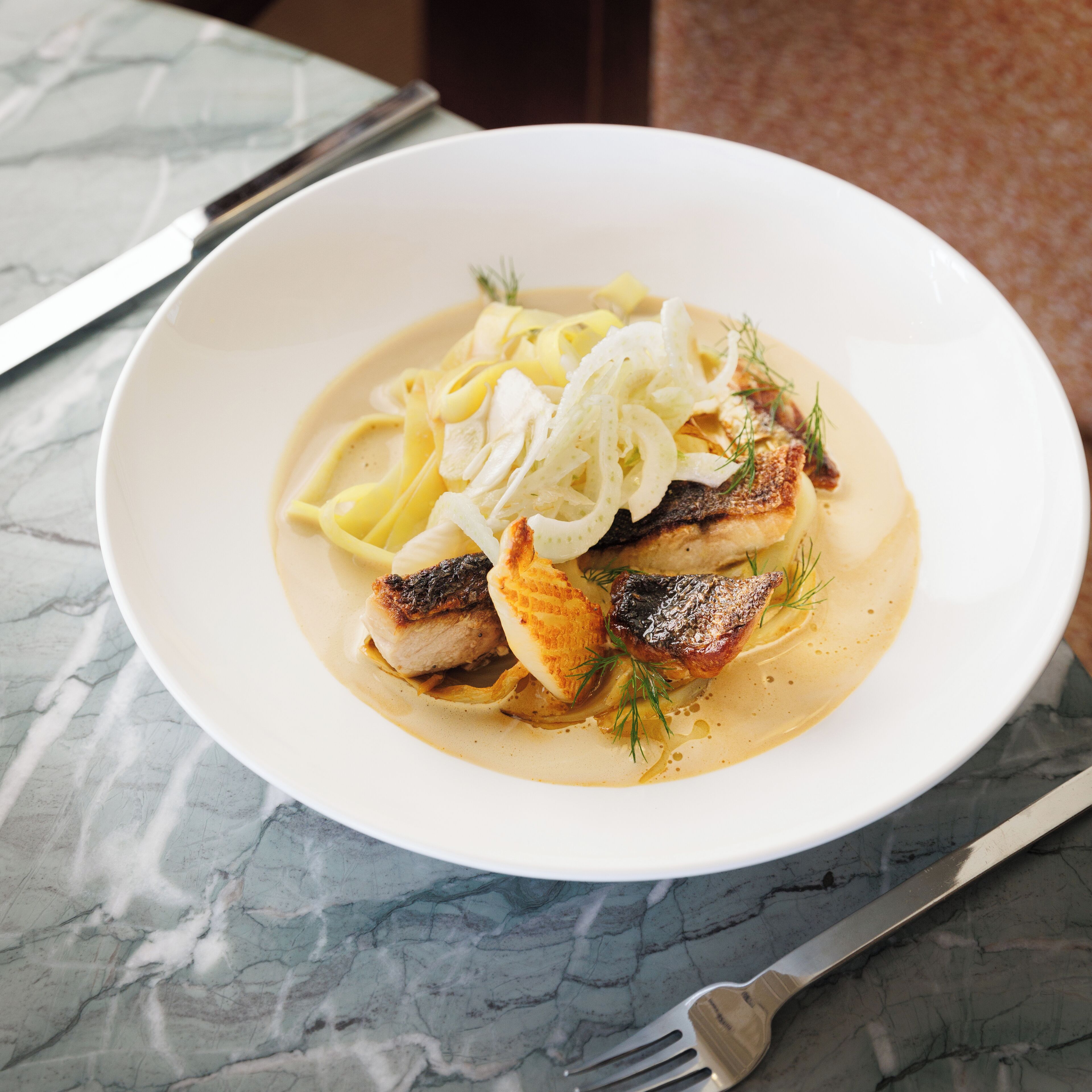 A plate of food with fish, noodles, and a creamy sauce, served on a white plate.