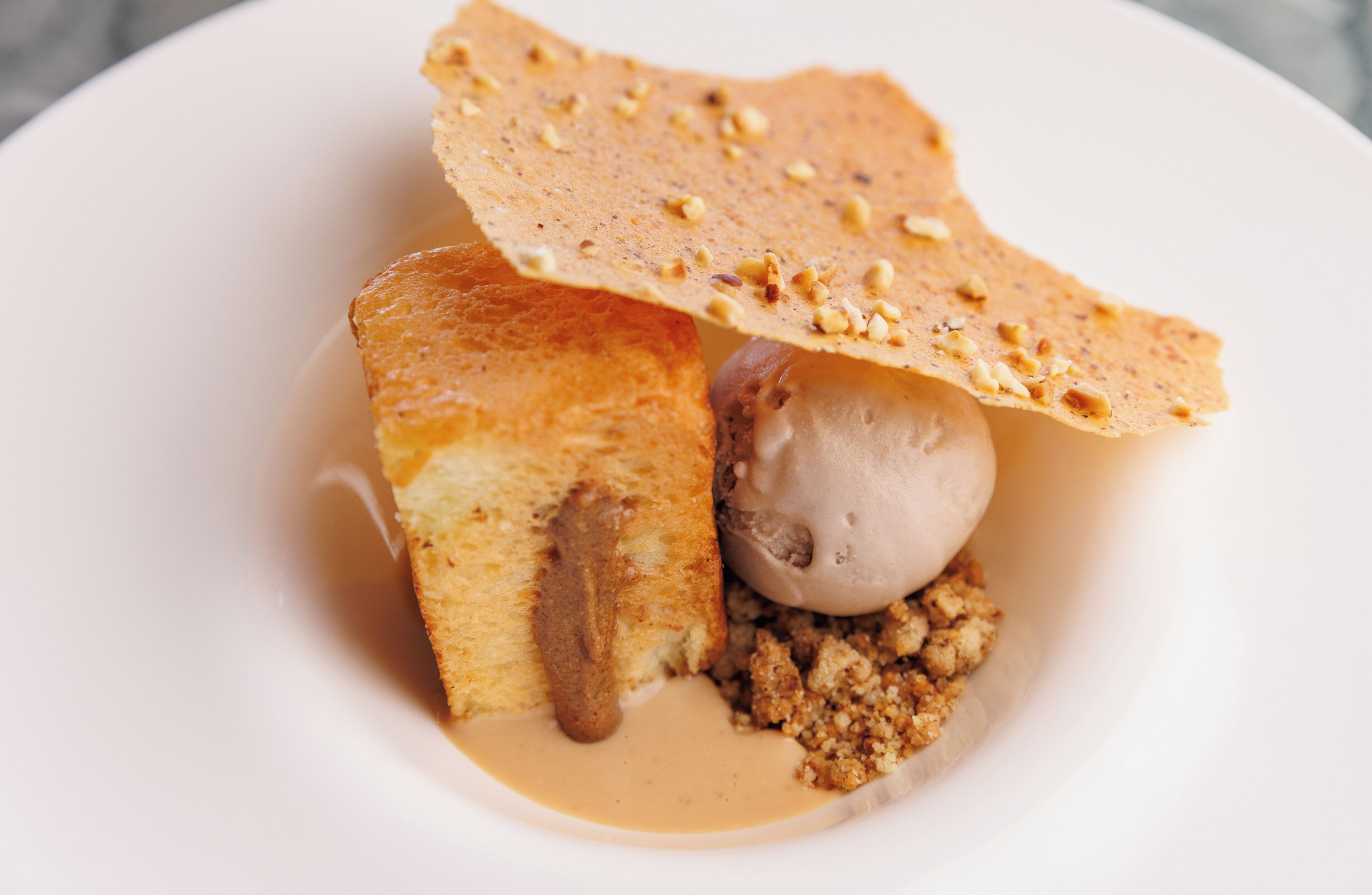 A dessert consisting of a piece of cake, a scoop of ice cream, and a crispy wafer.
