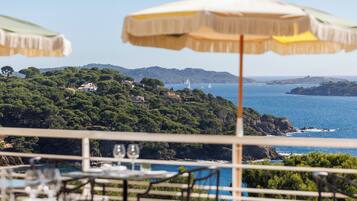 Una terraza con asientos al aire libre, con vistas a un paisaje costero con árboles y el mar.