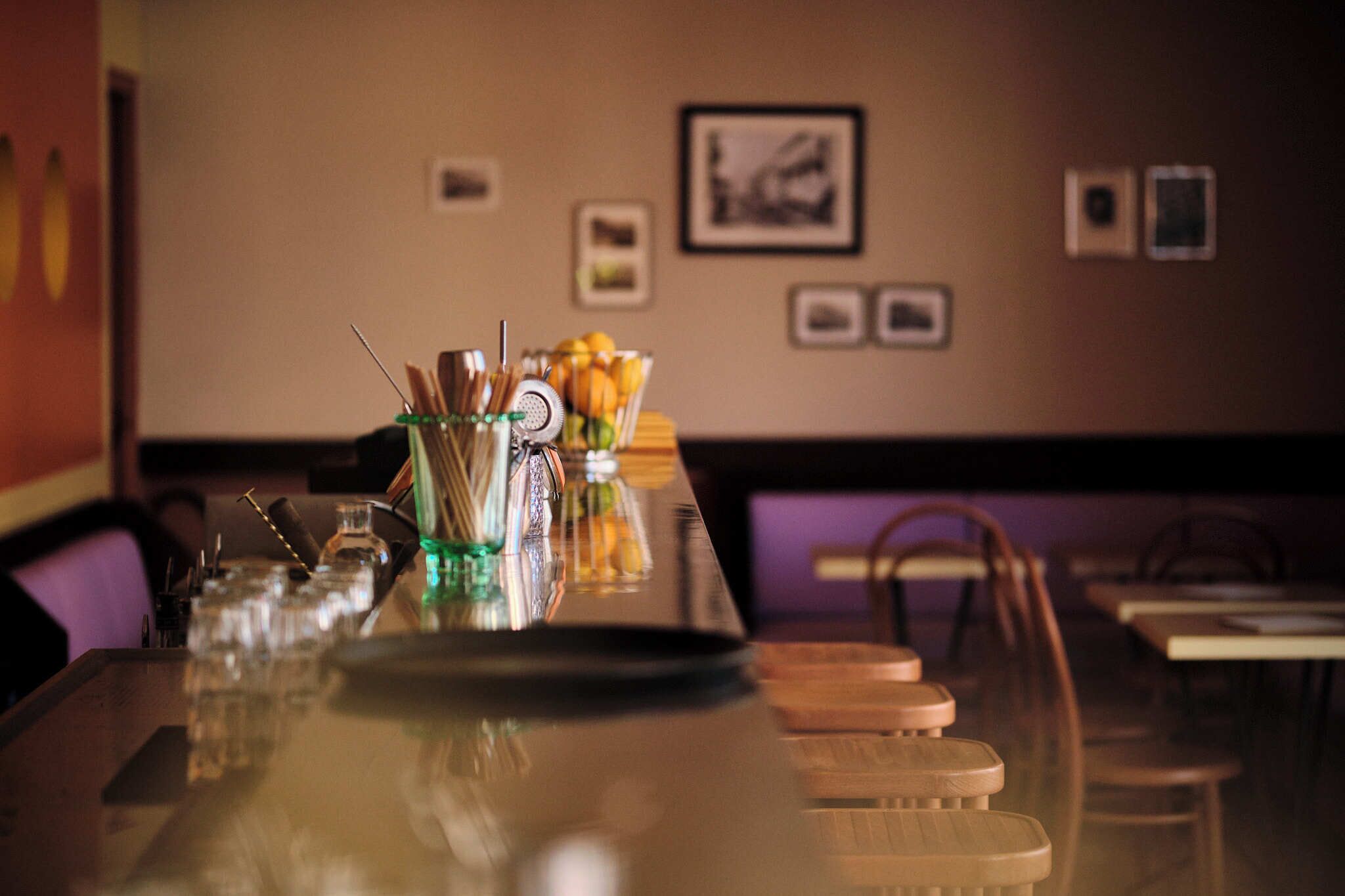 Un espace bar avec un long comptoir, des verres et un panier de fruits.
