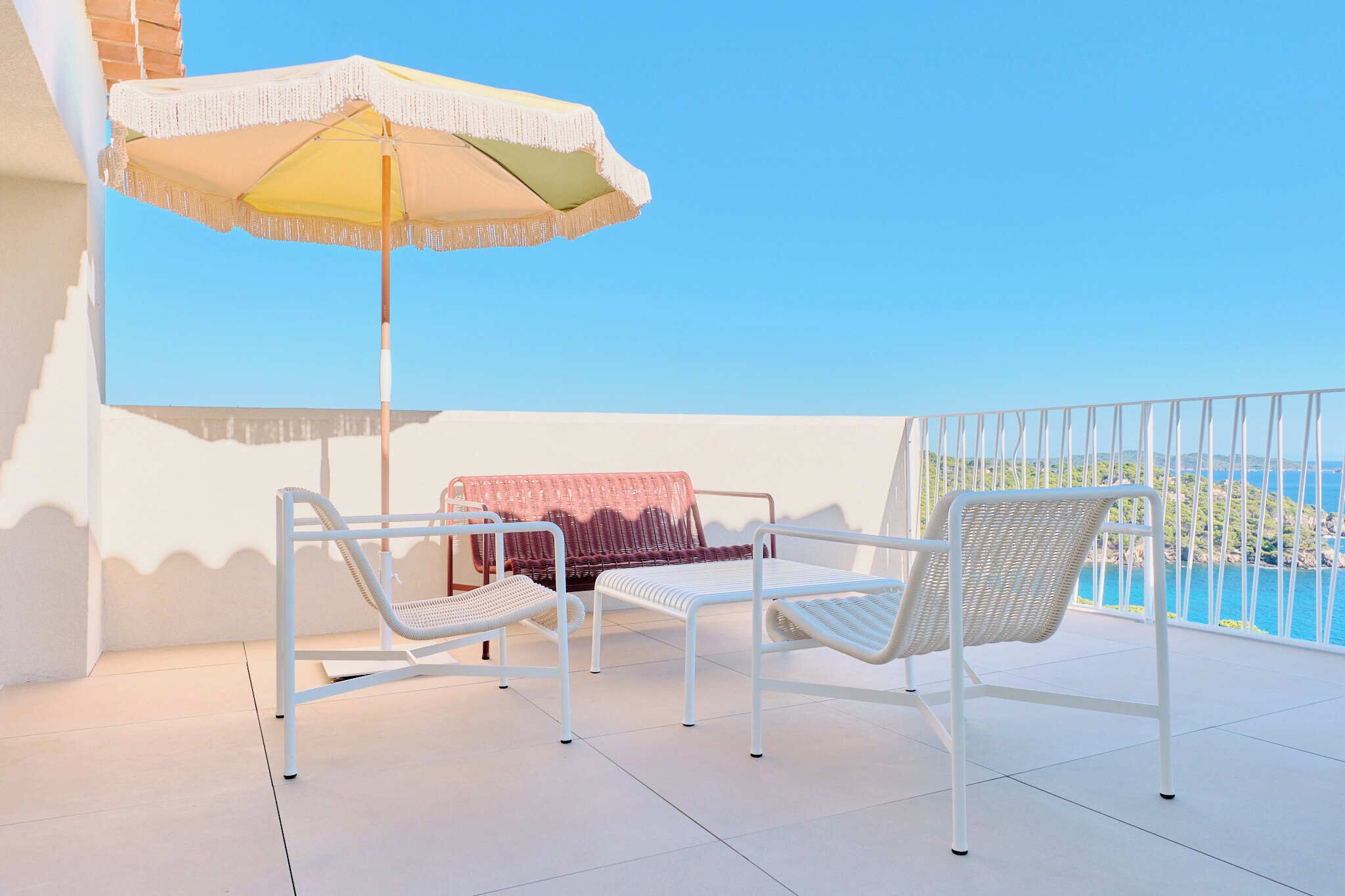 A balcony with white wicker chairs, a white umbrella, and a view of the sea.