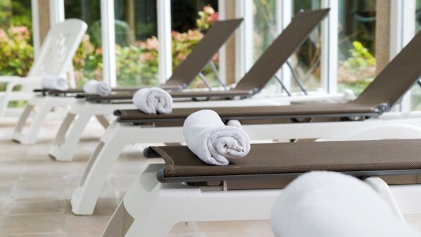 A row of sun loungers with towels, white chairs, and a view of greenery.