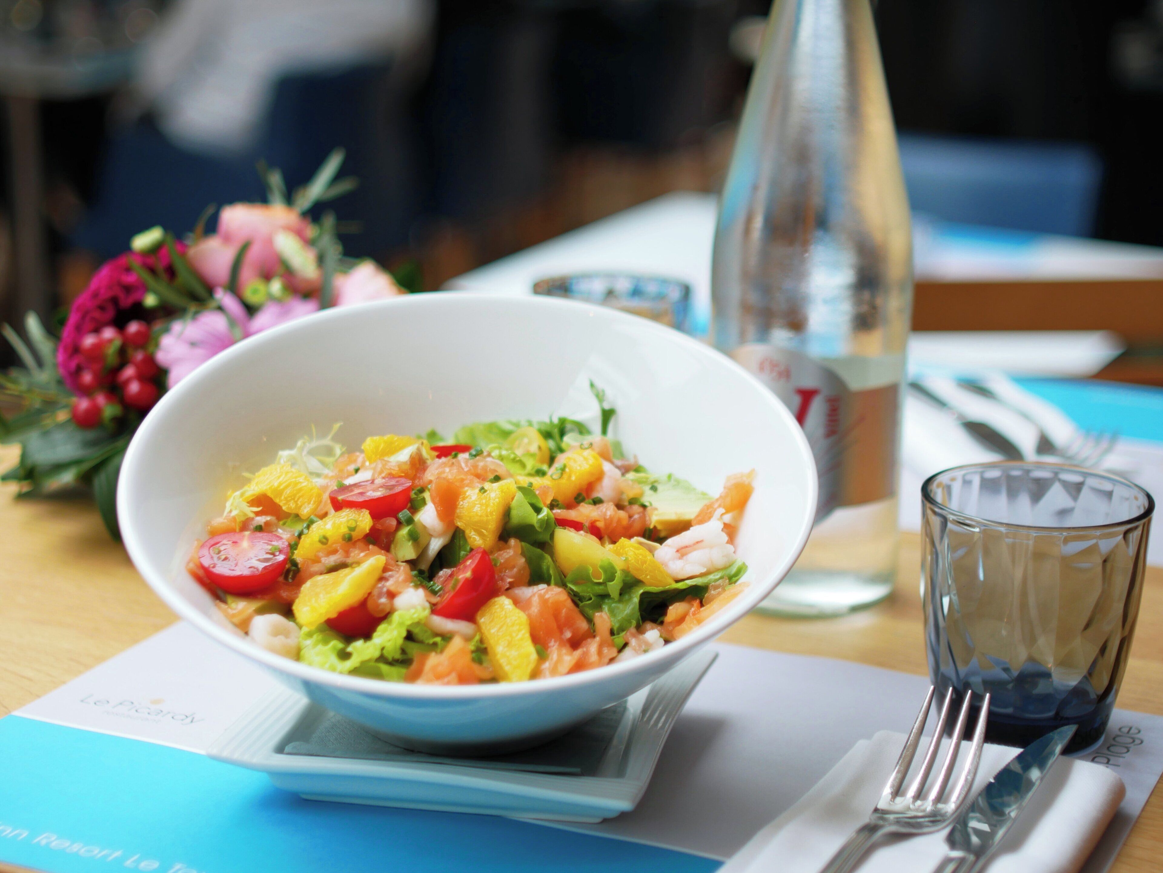 Un bol de salade sur une table, avec un verre d’eau et une fourchette.