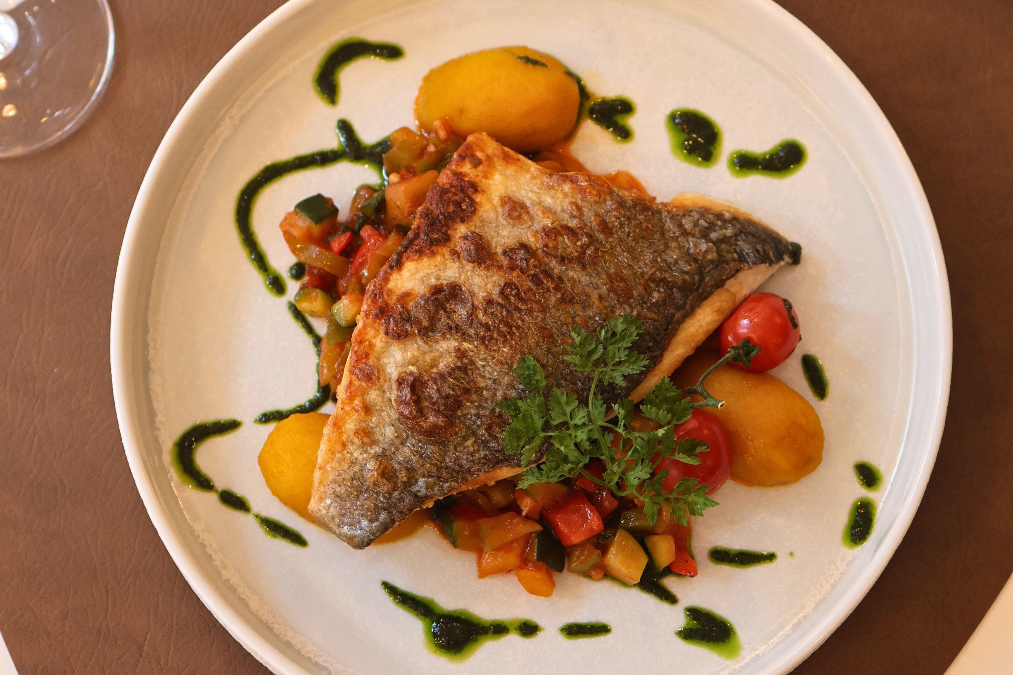 Un plato con un pescado a la parrilla, verduras y una guarnición sobre un plato blanco.