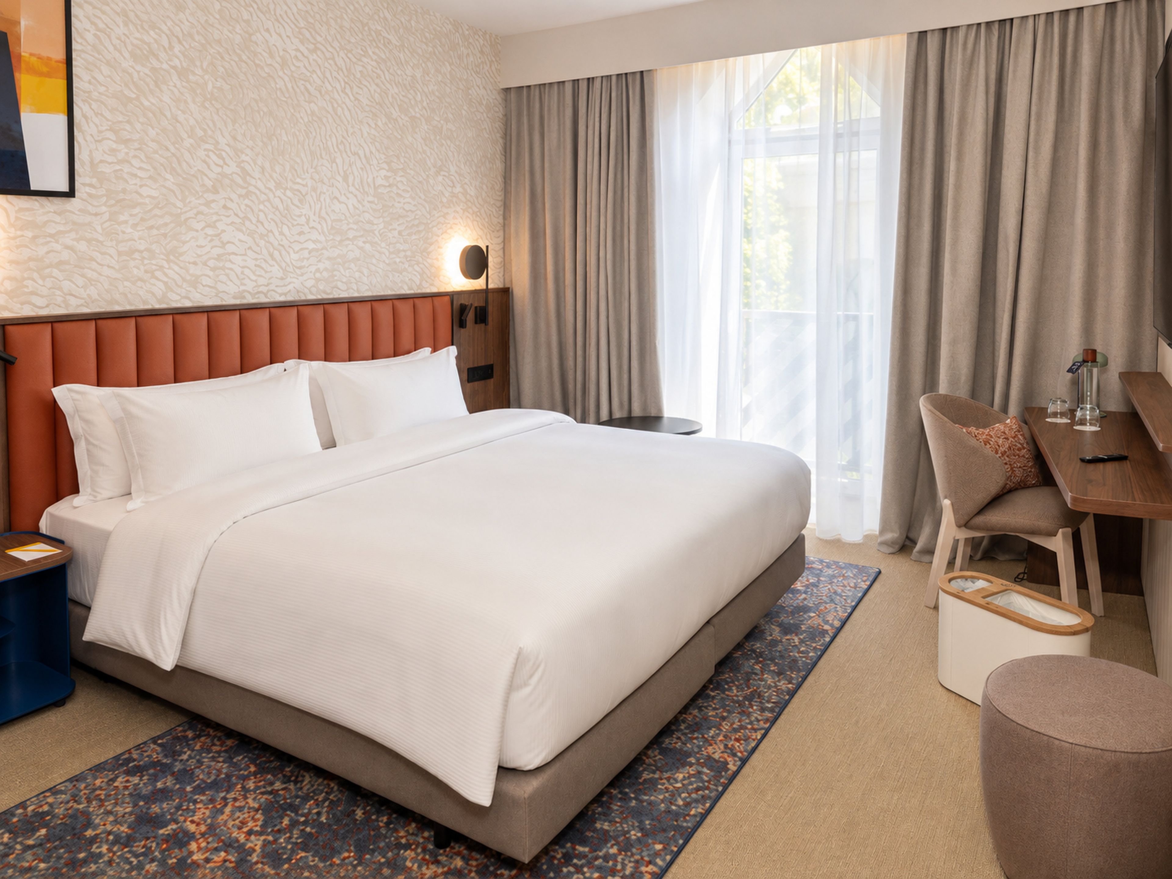Habitació d'hotel amb un llit gran, una taula, una cadira i una finestra amb cortines.