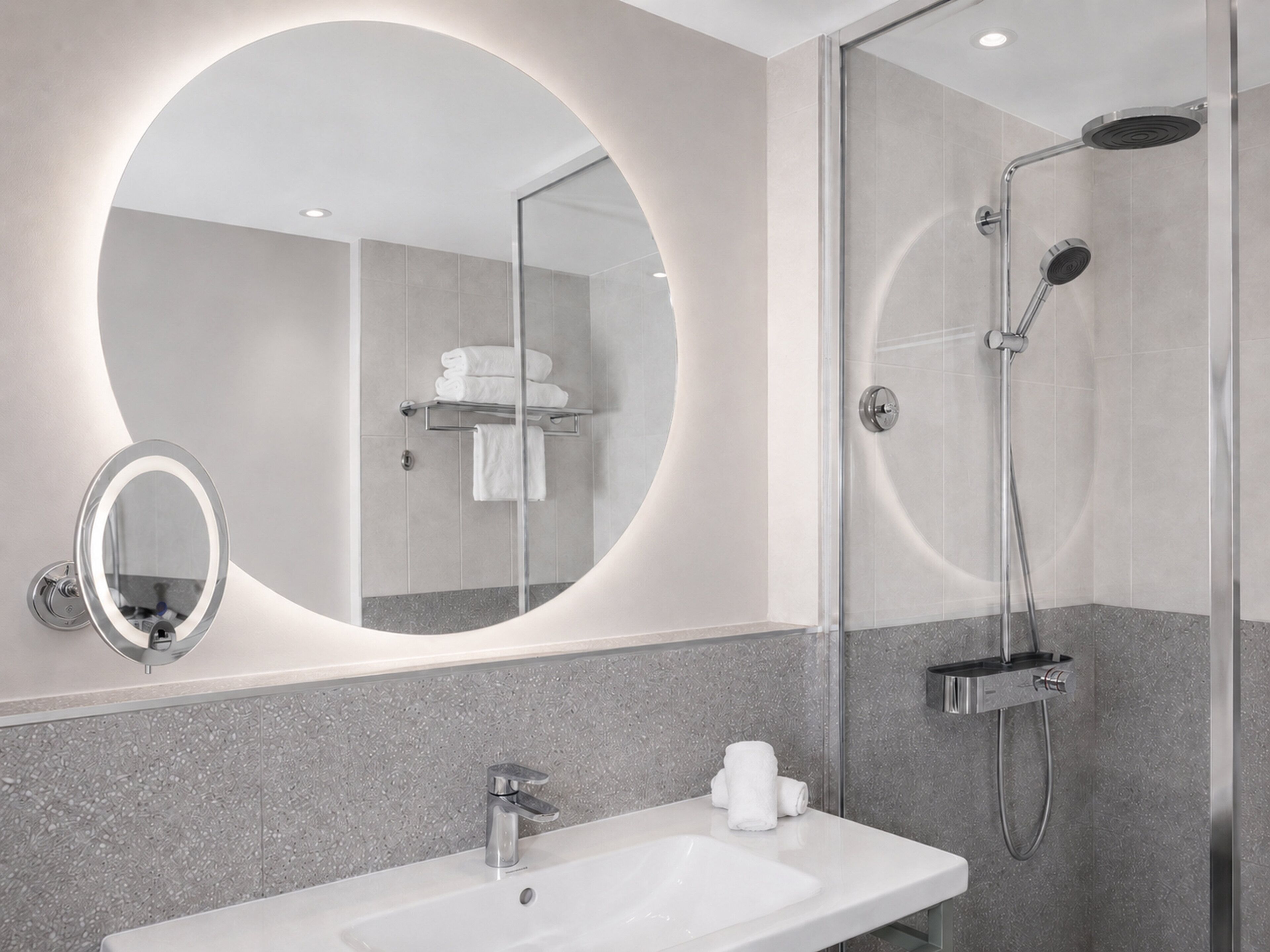 Une salle de bain moderne avec un miroir rond, un lavabo et une douche.