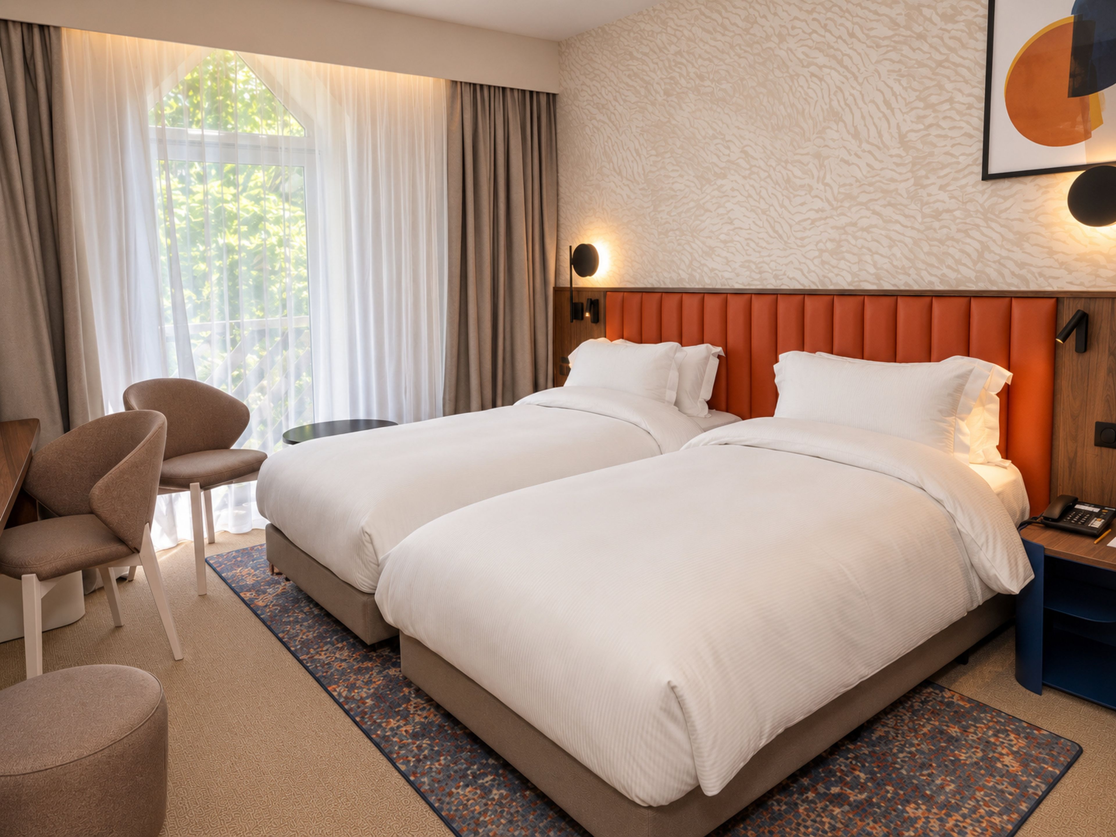 Une chambre d’hôtel avec deux lits, un coin salon comprenant une chaise, une petite table et une table de chevet avec un téléphone.