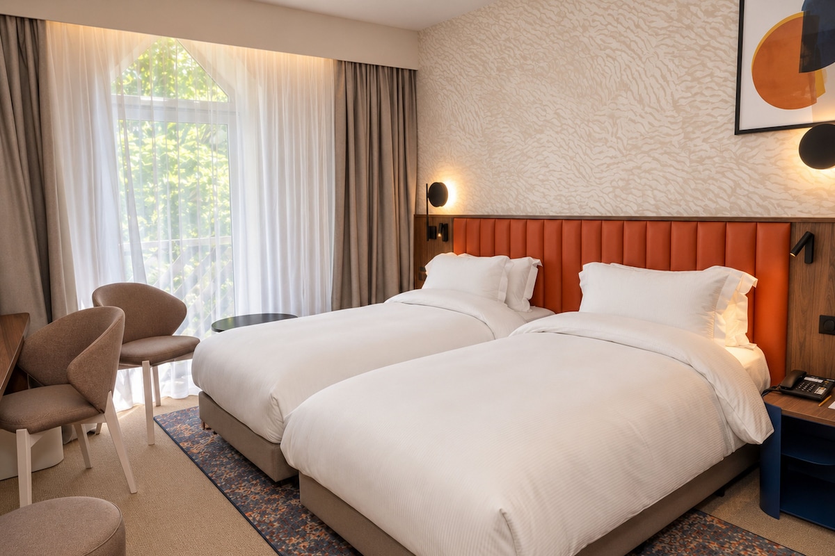 Een hotelkamer met twee bedden, een zithoek met een fauteuil, een klein tafeltje en een nachtkastje met een telefoon.