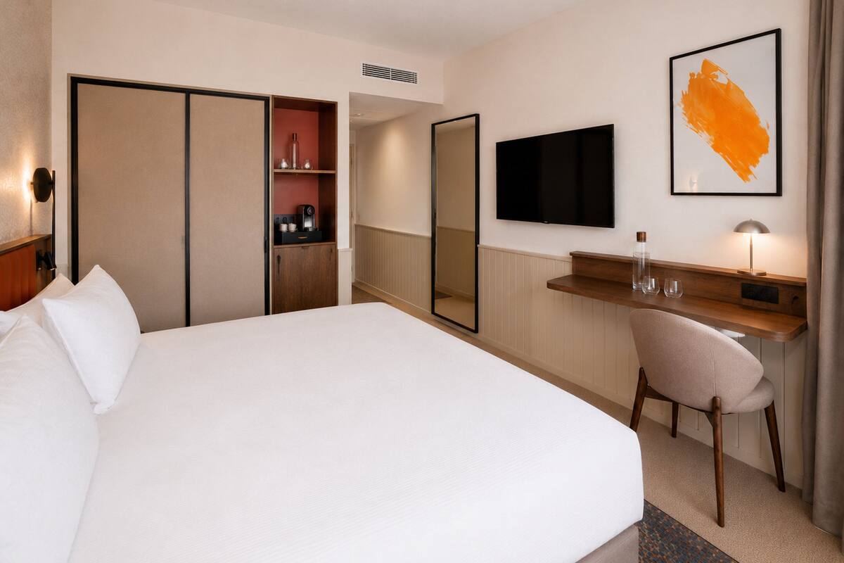 Ein Hotelzimmer mit einem Bett, einem Schreibtisch, einem Sessel, einem Fernseher und einem Spiegel.