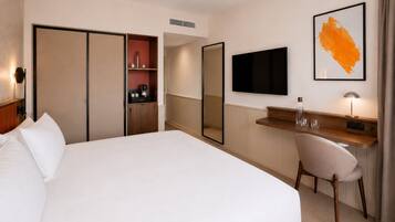 Habitación de hotel con cama, escritorio, silla, televisión y espejo.