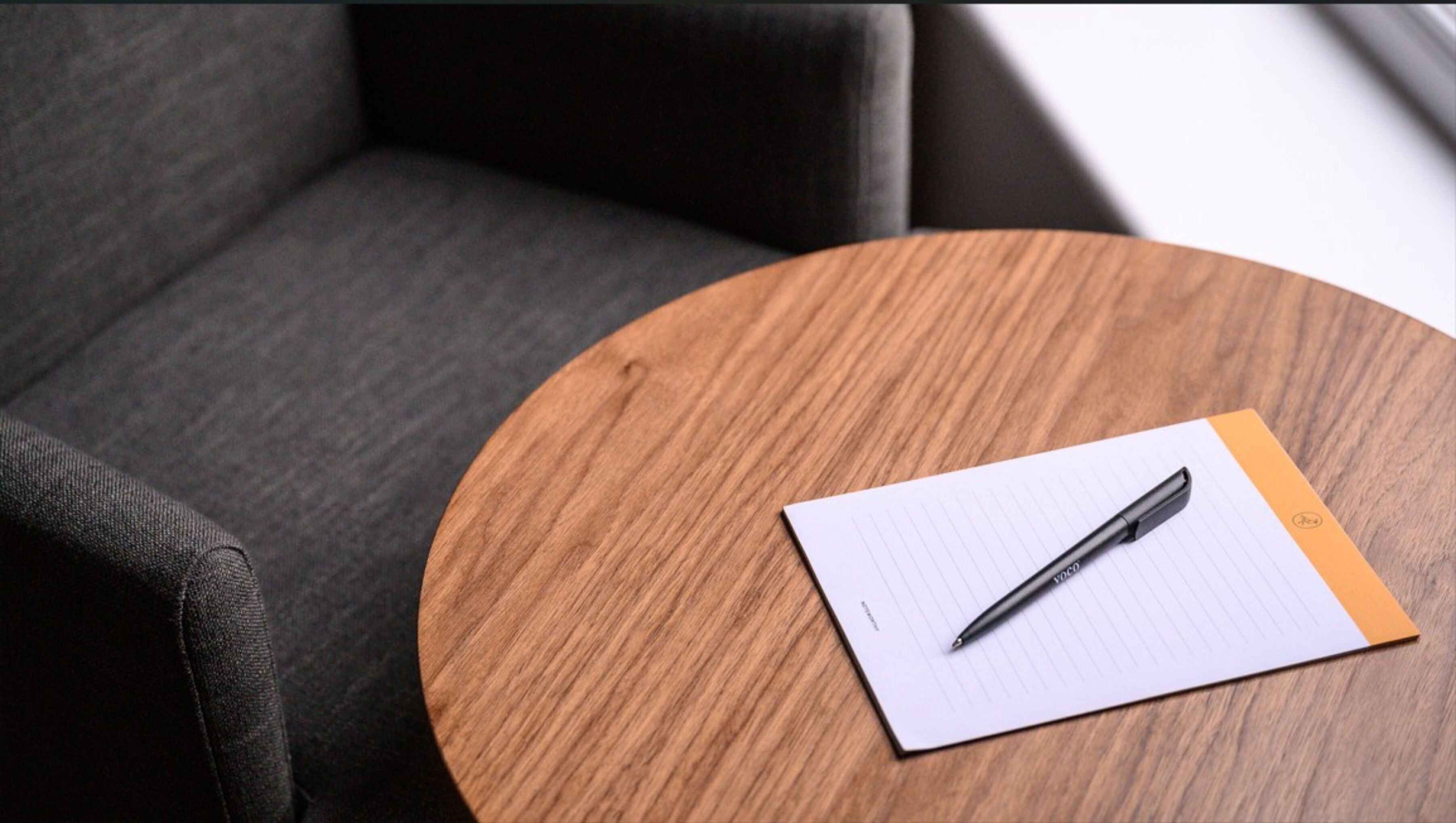 A round wooden table with a notepad and pen on it.