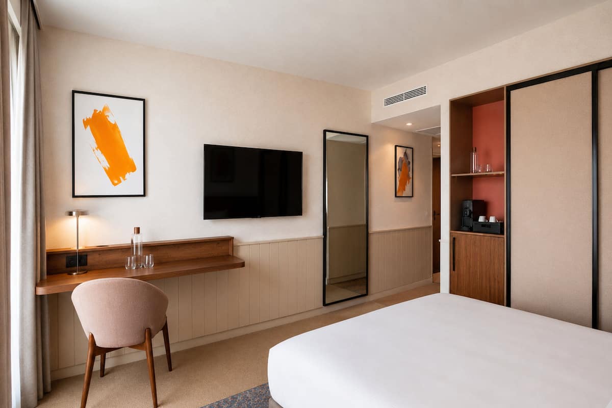Ein Hotelzimmer mit einem Bett, einem Schreibtisch mit Stuhl, einem Fernseher, einem großen Spiegel und einem Kleiderschrank.