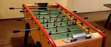 A foosball table with a wooden base and red accents, set on a carpeted floor in a room with beige walls.