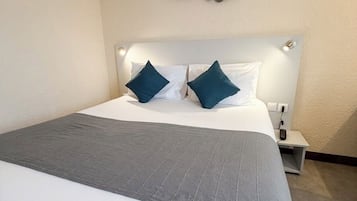 A neatly made bed with a grey blanket and two pillows, a bedside table with a lamp, and a wall art piece above the bed.