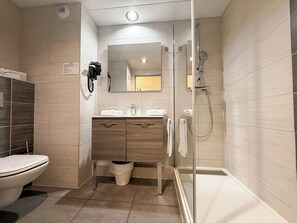 A modern bathroom with a toilet, vanity, mirror, and glass-enclosed shower.