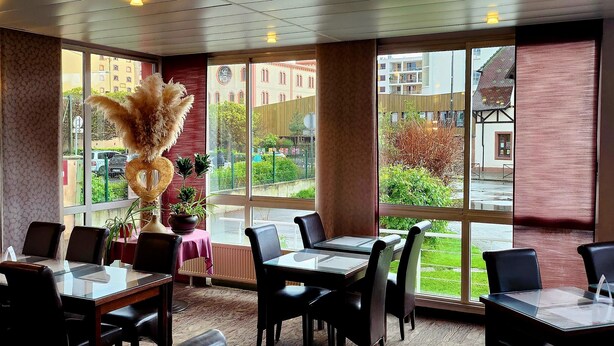 Un restaurant doté de nombreuses tables et chaises, de grandes fenêtres offrant une vue sur les bâtiments et la verdure environnante.