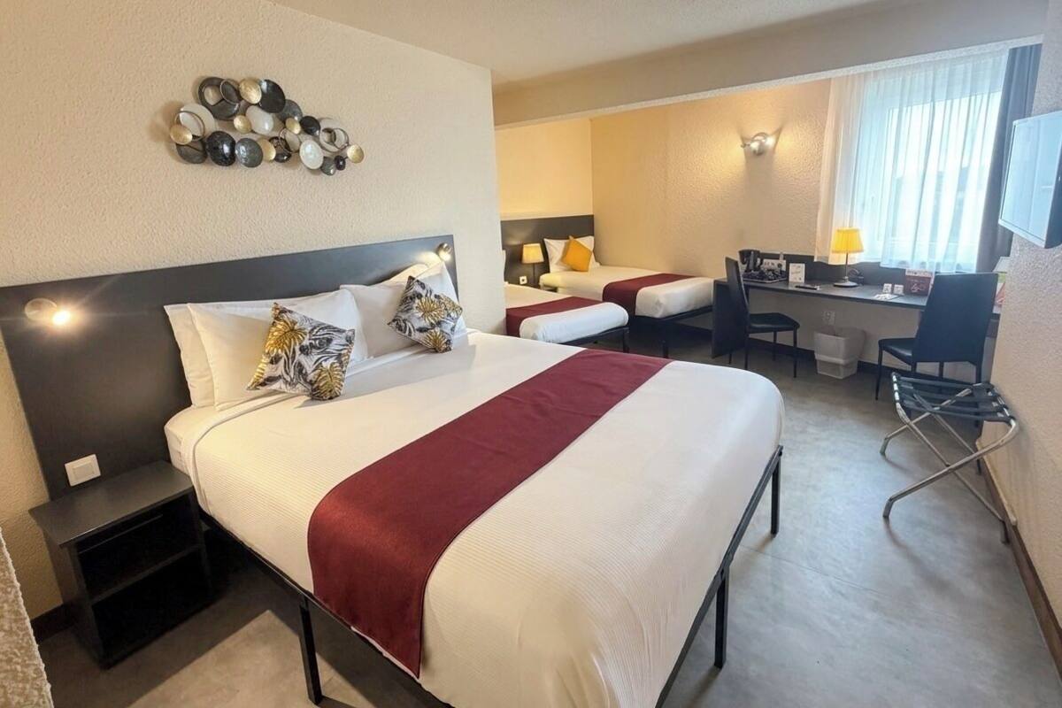 Een hotelkamer met een groot bed, twee kleinere bedden, een bureau en een stoel.