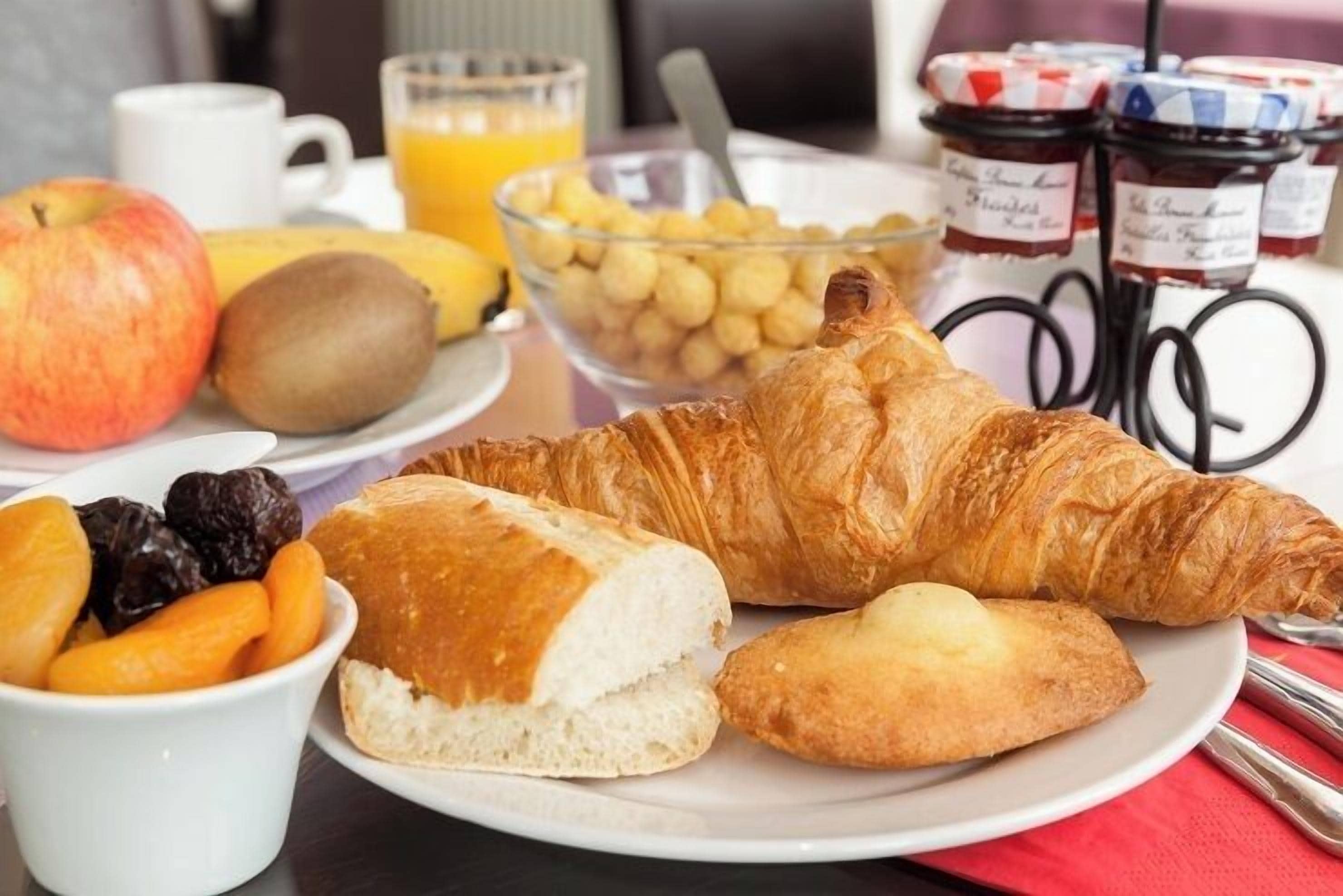 Une table dressée pour le petit-déjeuner, avec des croissants, des fruits et un verre de jus d’orange.
