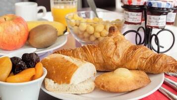 Une table dressée pour le petit-déjeuner, avec des croissants, des fruits et un verre de jus d’orange.