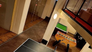 Une table de billard agrémentée d’un arrangement floral, une table de baby-foot et une bibliothèque remplie de livres.