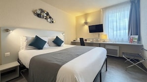 Une chambre d’hôtel équipée d’un lit, d’un bureau, d’une chaise, d’une télévision et d’une fenêtre avec des rideaux.