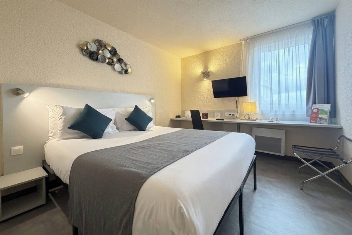 Een hotelkamer met een bed, bureau, stoel, televisie en raam met gordijnen.