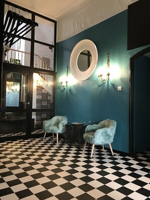 A room with a checkered floor, two fluffy chairs, a round mirror, and wall sconces. - Hotel Mystique (Bad Homburg v.d. Hoehe)
