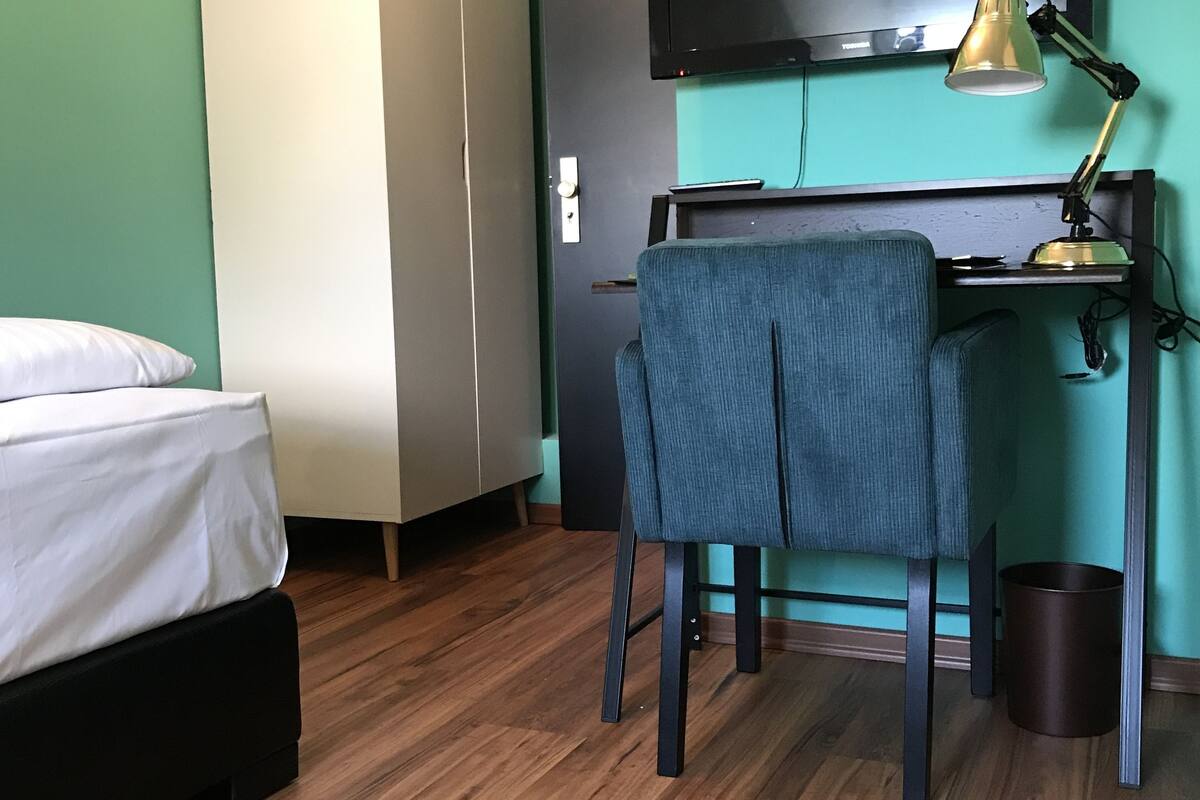 A room with a bed, a desk with a chair, a television, and a wardrobe.