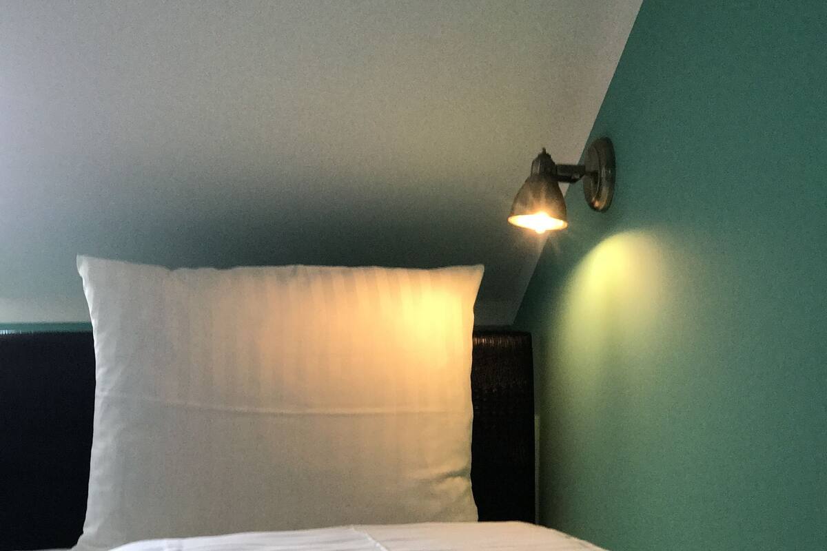 A neatly made bed with a pillow and a wall-mounted light fixture.