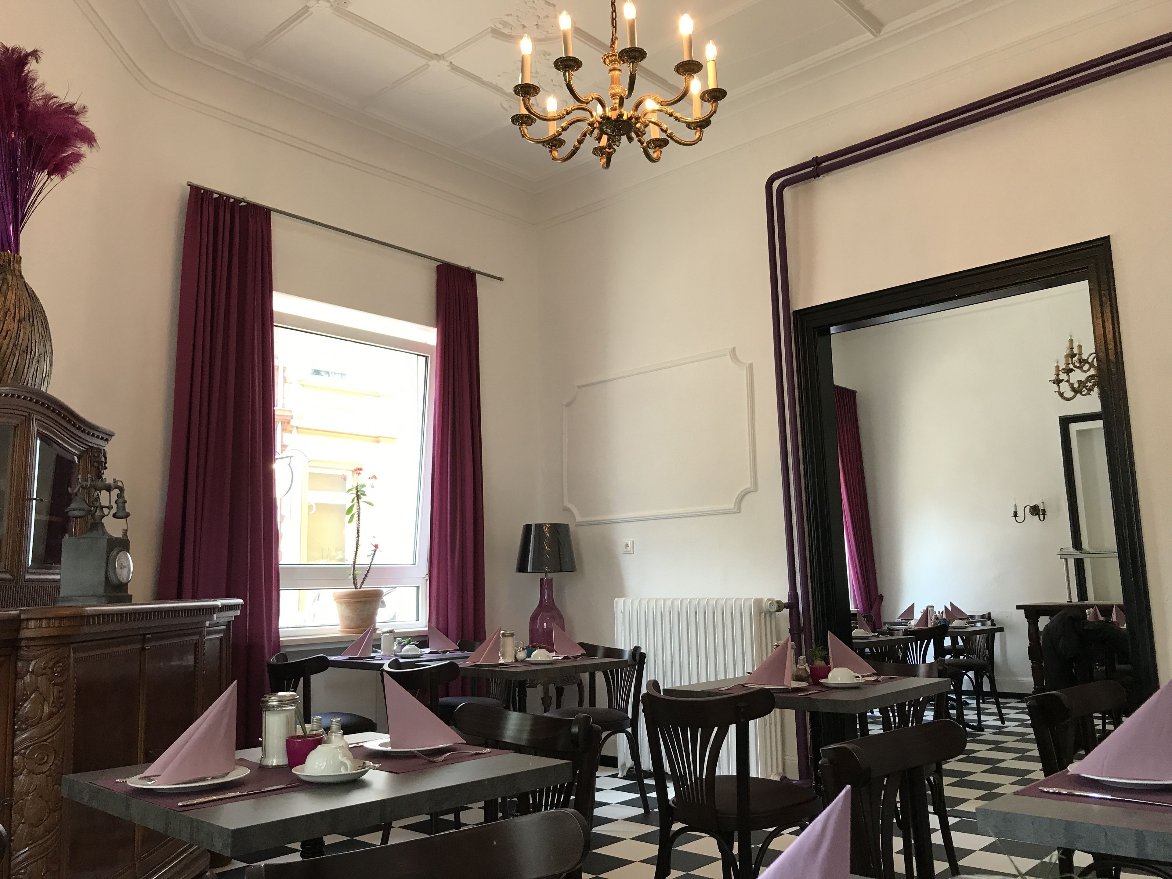 A dining area with tables set for service, a chandelier, and a large mirror on the wall.