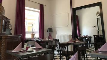 A dining area with tables set for service, a chandelier, and a large mirror on the wall.