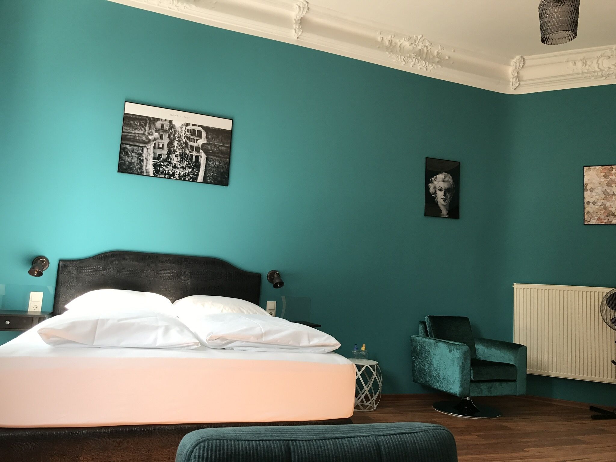 Ein Schlafzimmer mit einem Bett, einem Sessel, einem Heizkörper und Wandbildern.