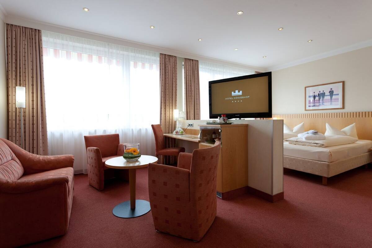 A hotel room with a bed, a desk with a television, a small table with a vase of flowers, and a sofa.