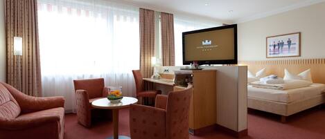 Habitación de hotel con cama, escritorio con televisor, mesita con un florero y un sofá.