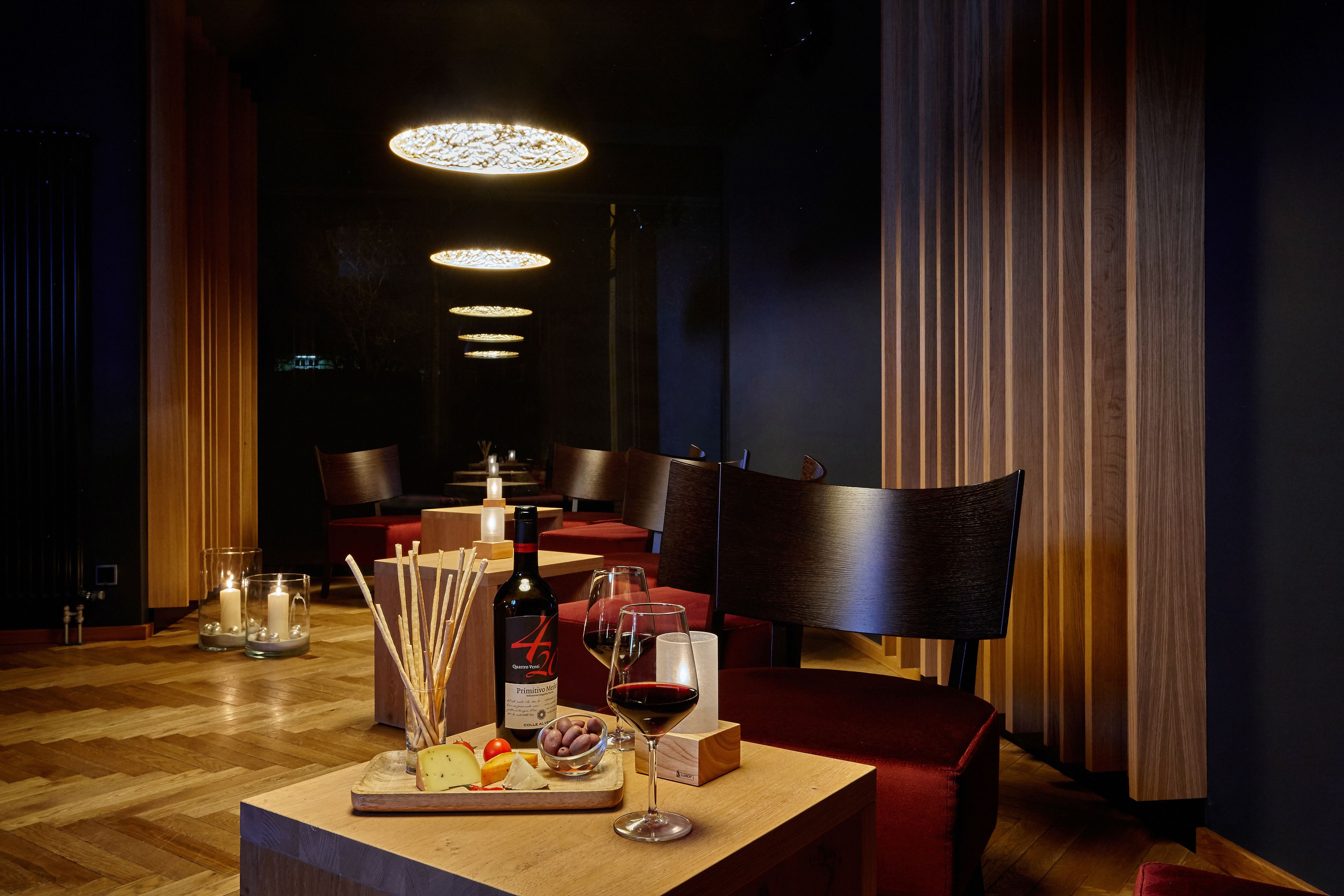 Interior de restaurante con una mesa de madera preparada para dos personas, que incluye una botella de vino, copas y una bandeja de frutas.