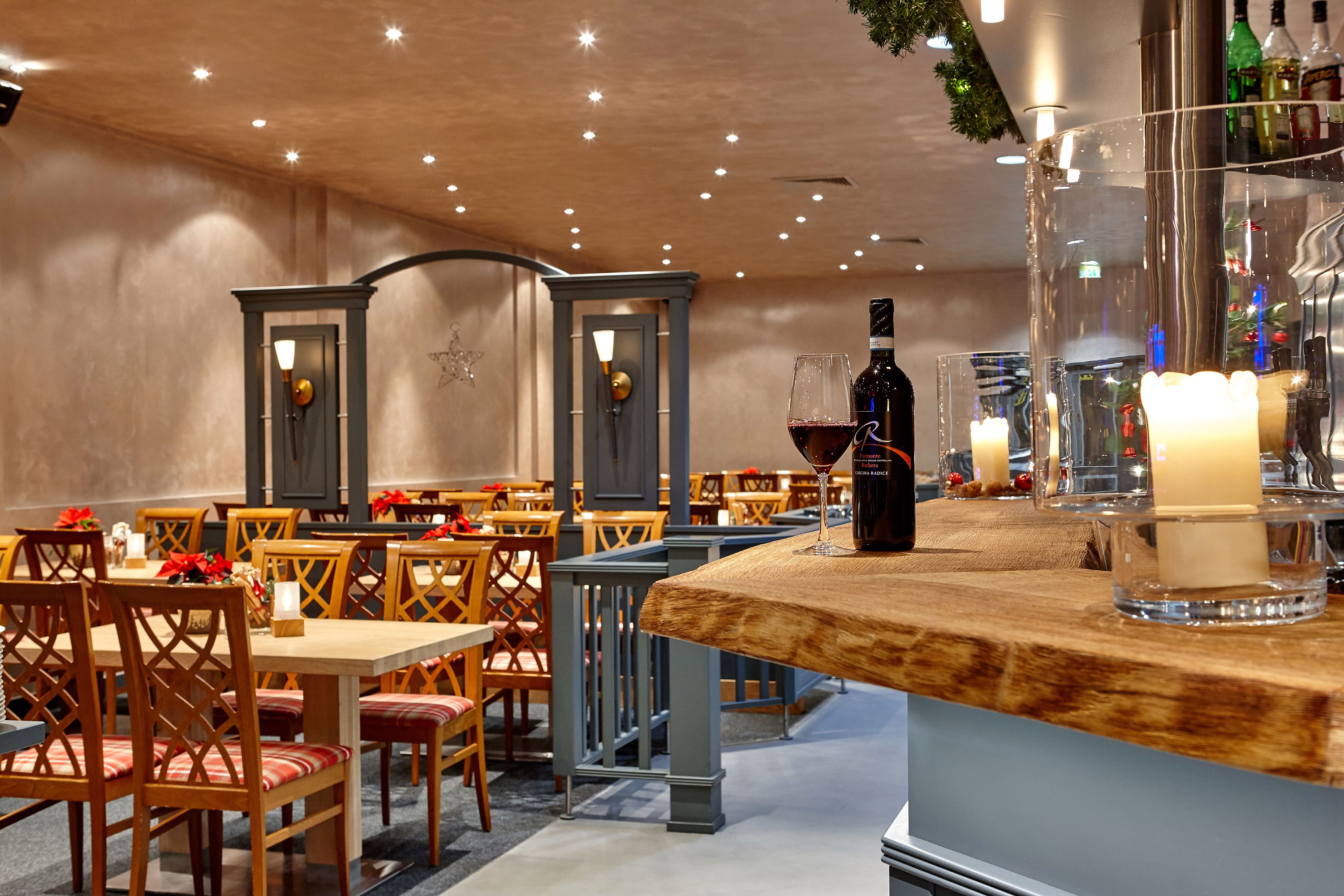 A restaurant with wooden tables and chairs, a bar area with a bottle of wine and glasses, and candles on the counter.