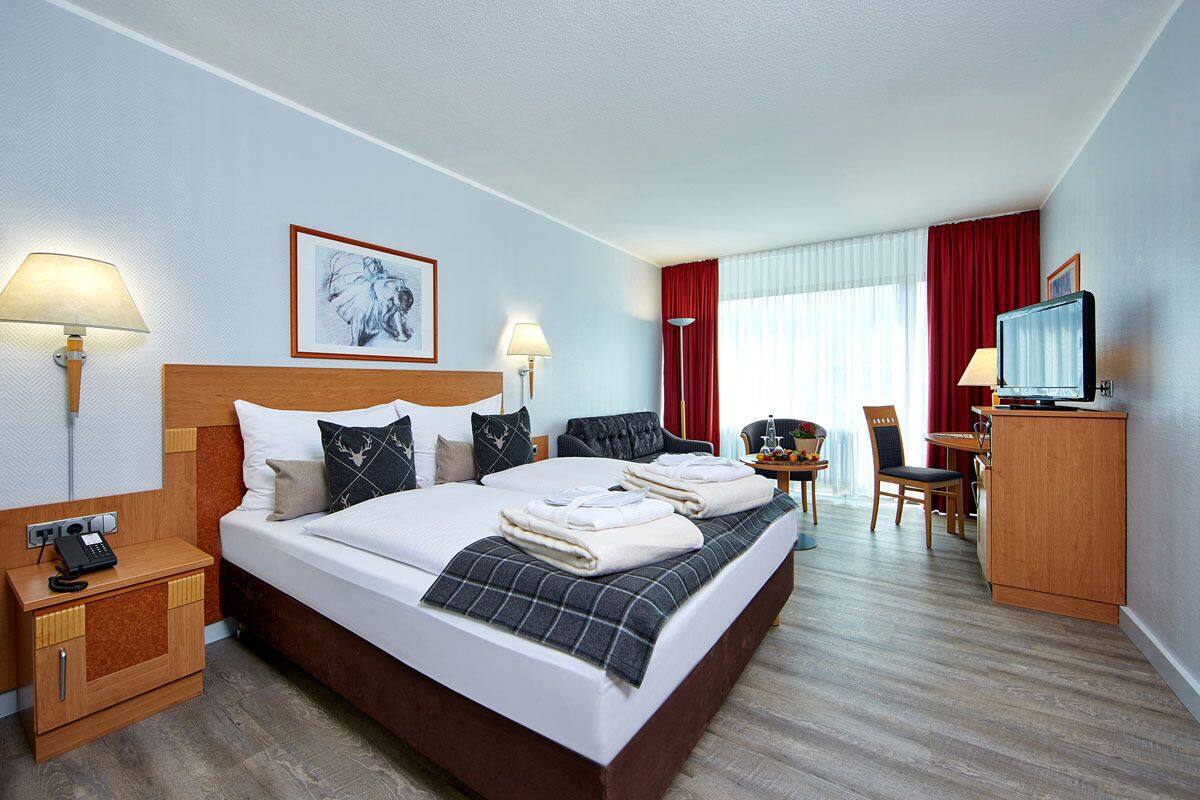 A hotel room with a large bed, bedside lamps, a desk with a chair, a television, and a red curtain.