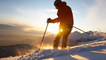 Una persona esquiando en una montaña nevada con el sol poniéndose al fondo.