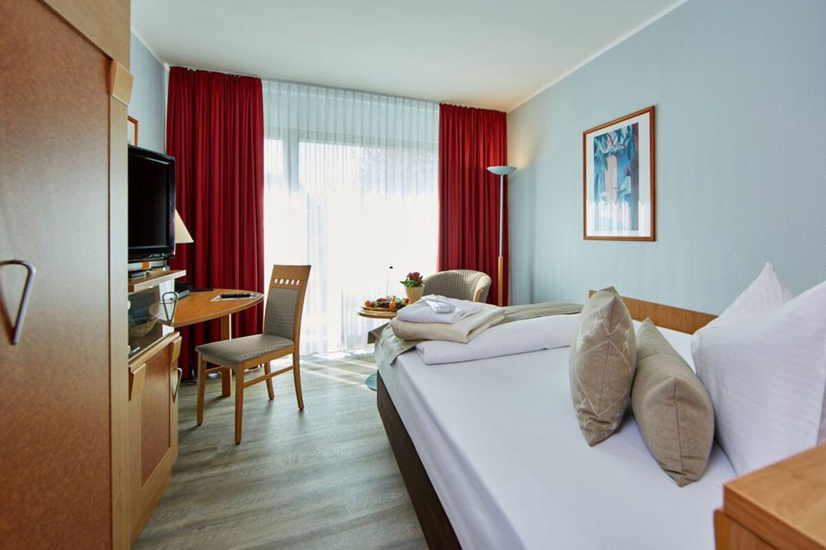 A hotel room with a bed, a desk, a television, and a chair.