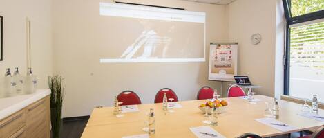 A conference room with a long table, red chairs, a projector screen, and a whiteboard.