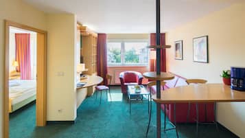 A hotel room with a bed, a desk, a dining table, chairs, a sofa, a window, and a radiator.