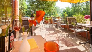 Une terrasse extérieure avec des tables et des chaises, un parasol jaune et des plantes en pot.