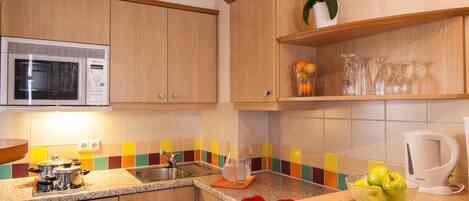 Una cocina con armarios de madera, un microondas, un lavabo y una encimera con un frutero y un plato de pimientos rojos.