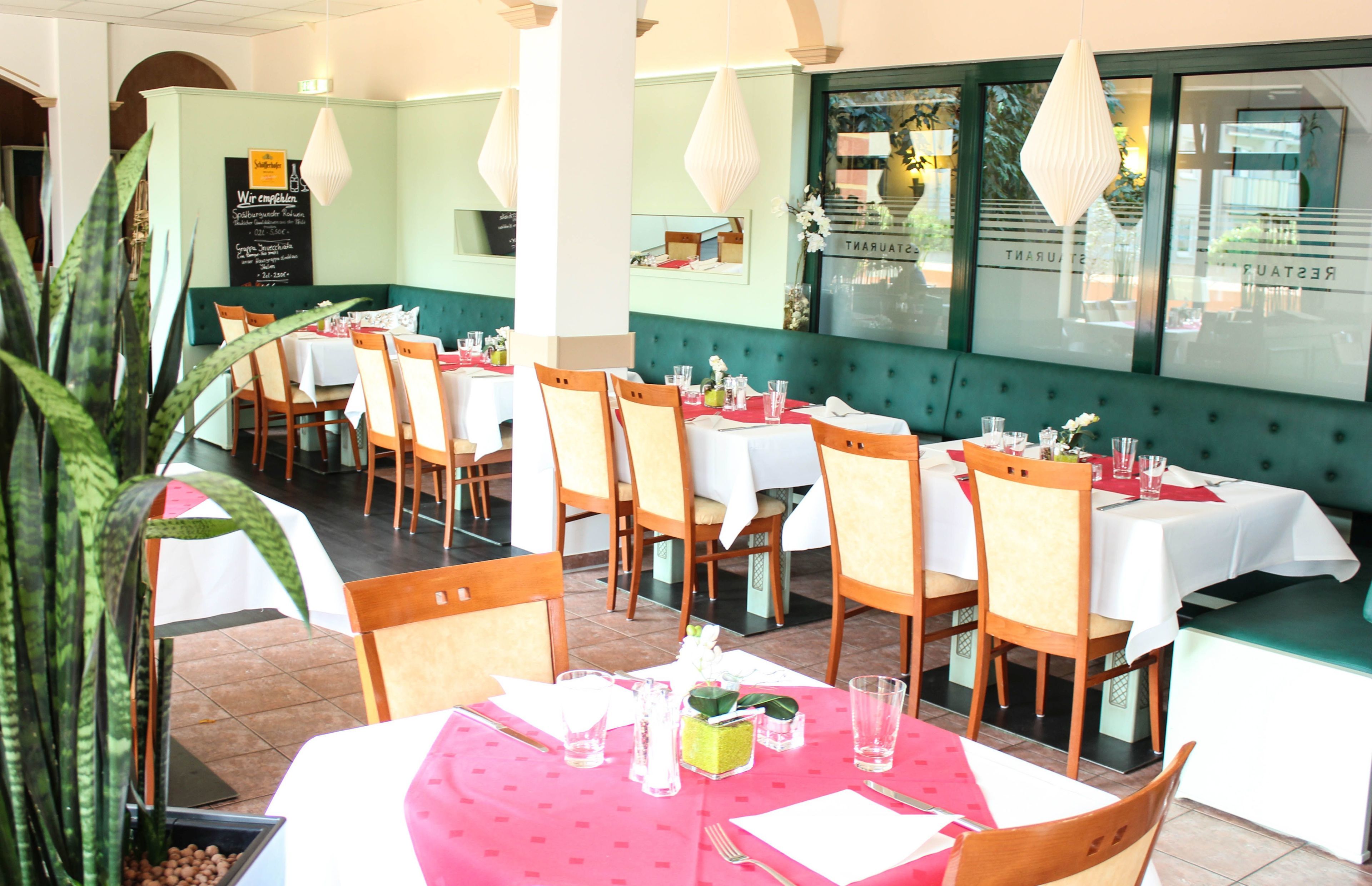 Un restaurante con varias mesas y sillas, un banco acolchado verde y un menú en una pizarra.