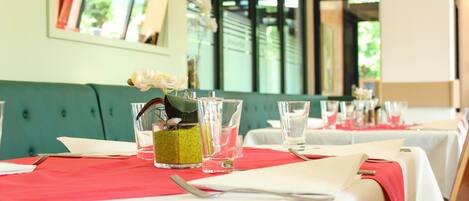 A dining area with tables set for two, featuring white tablecloths and red napkins.