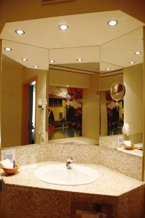 A bathroom with a large mirror, a sink, and a ceiling with recessed lighting. - Suite Hotel Leipzig (Leipzig)