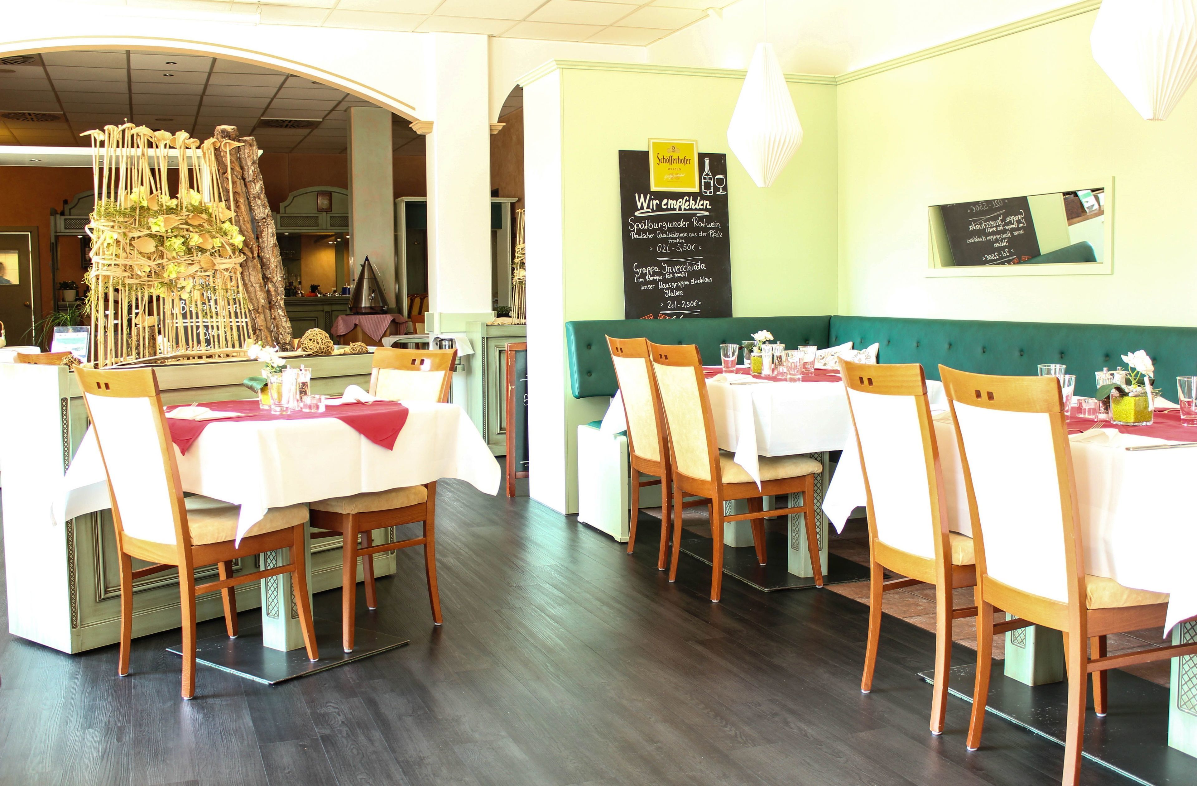 Un ristorante con sedie e tavoli di legno, un menu alla lavagna e una struttura decorativa con piante.